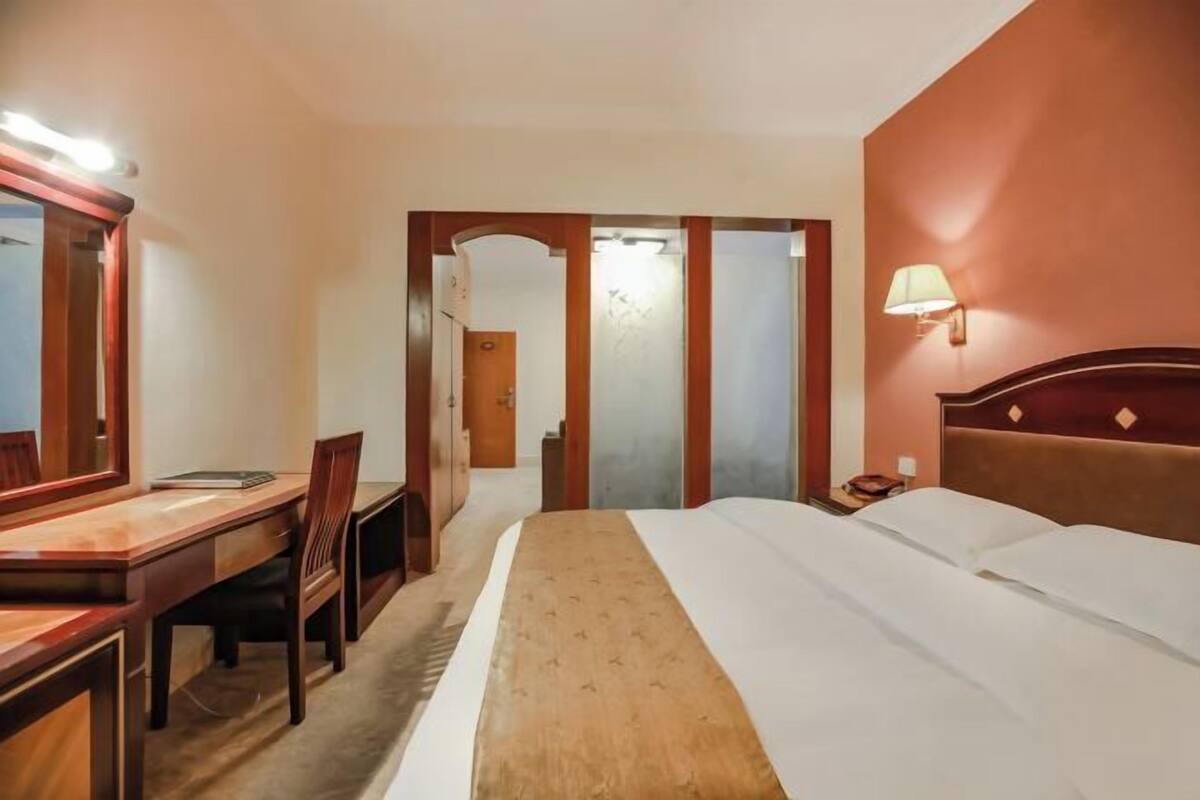 A hotel room with a bed, a desk with a chair, a nightstand, and a lamp.