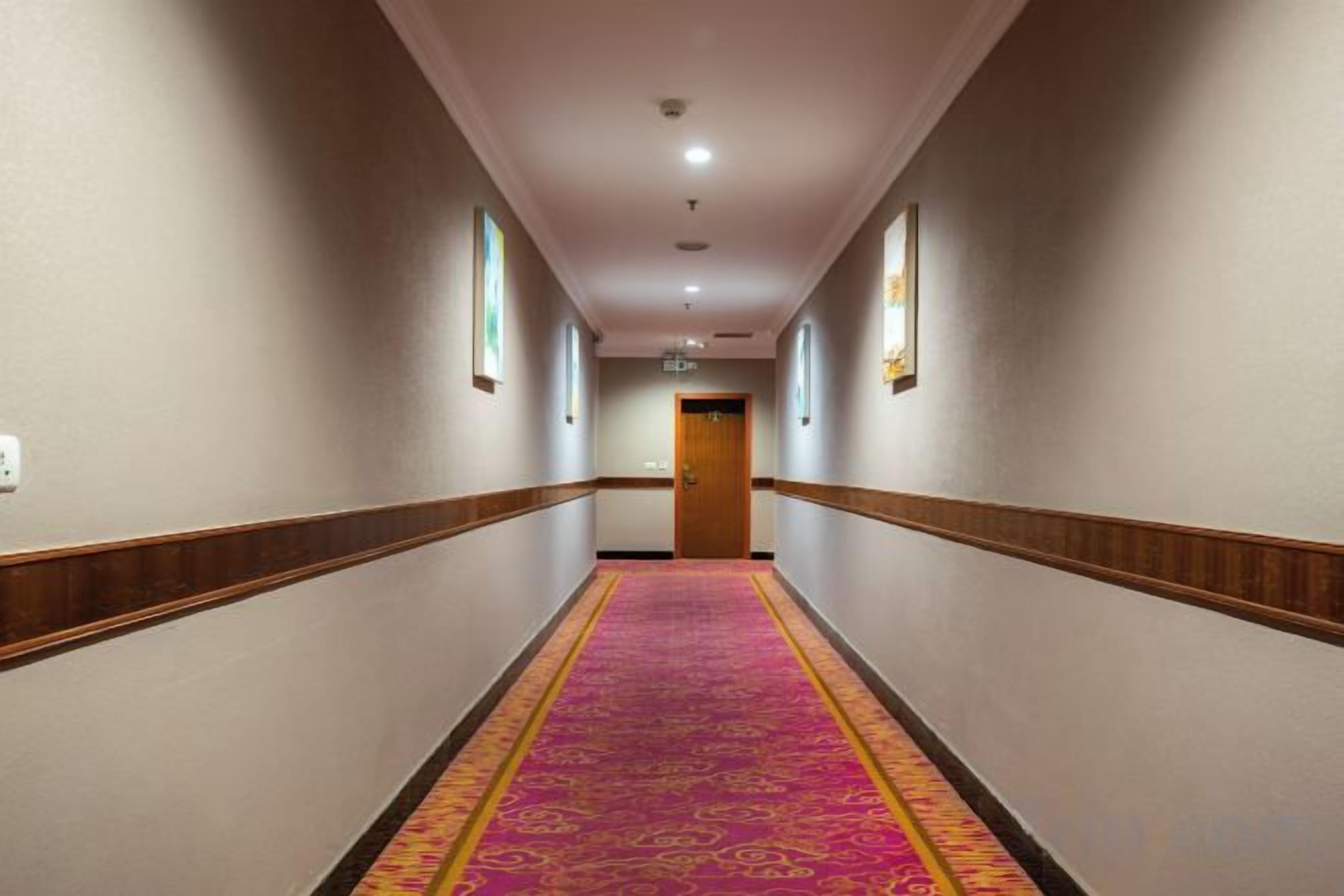 Un pasillo de hotel con piso alfombrado, detalles de madera y cuadros en las paredes.