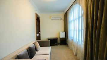 A room with a sofa, a small table, a TV, and a window with curtains.