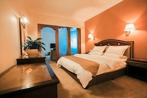 A hotel room with a bed, bedside tables, a lamp, a plant, and a mirror. - Libo Dapeng Business Hotel (Libo Ancient Town) (Libo)