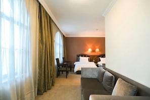 A hotel room with a bed, a sofa, a desk, and a chair. There is a window with curtains, a lamp on the desk, and a wall-mounted light. - Libo Dapeng Business Hotel (Libo Ancient Town) (Libo)
