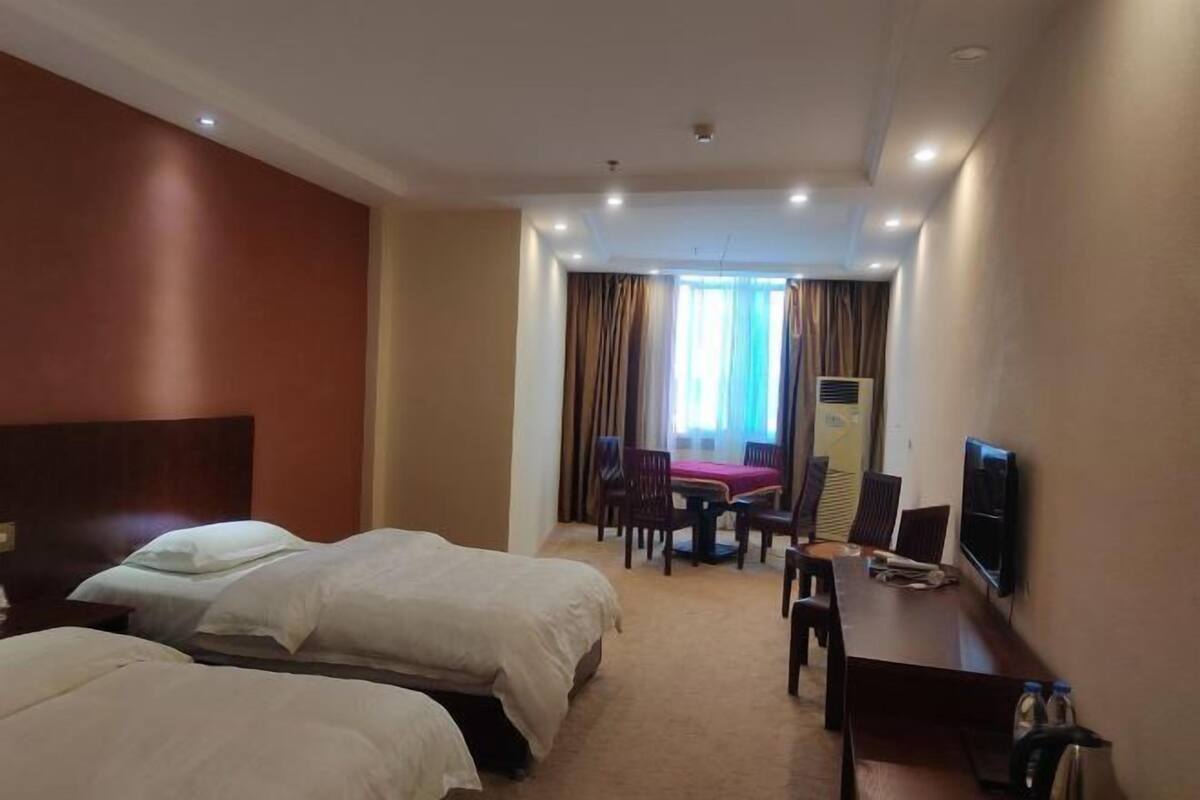 A hotel room with two beds, a desk with a chair, a television, and a window with curtains.