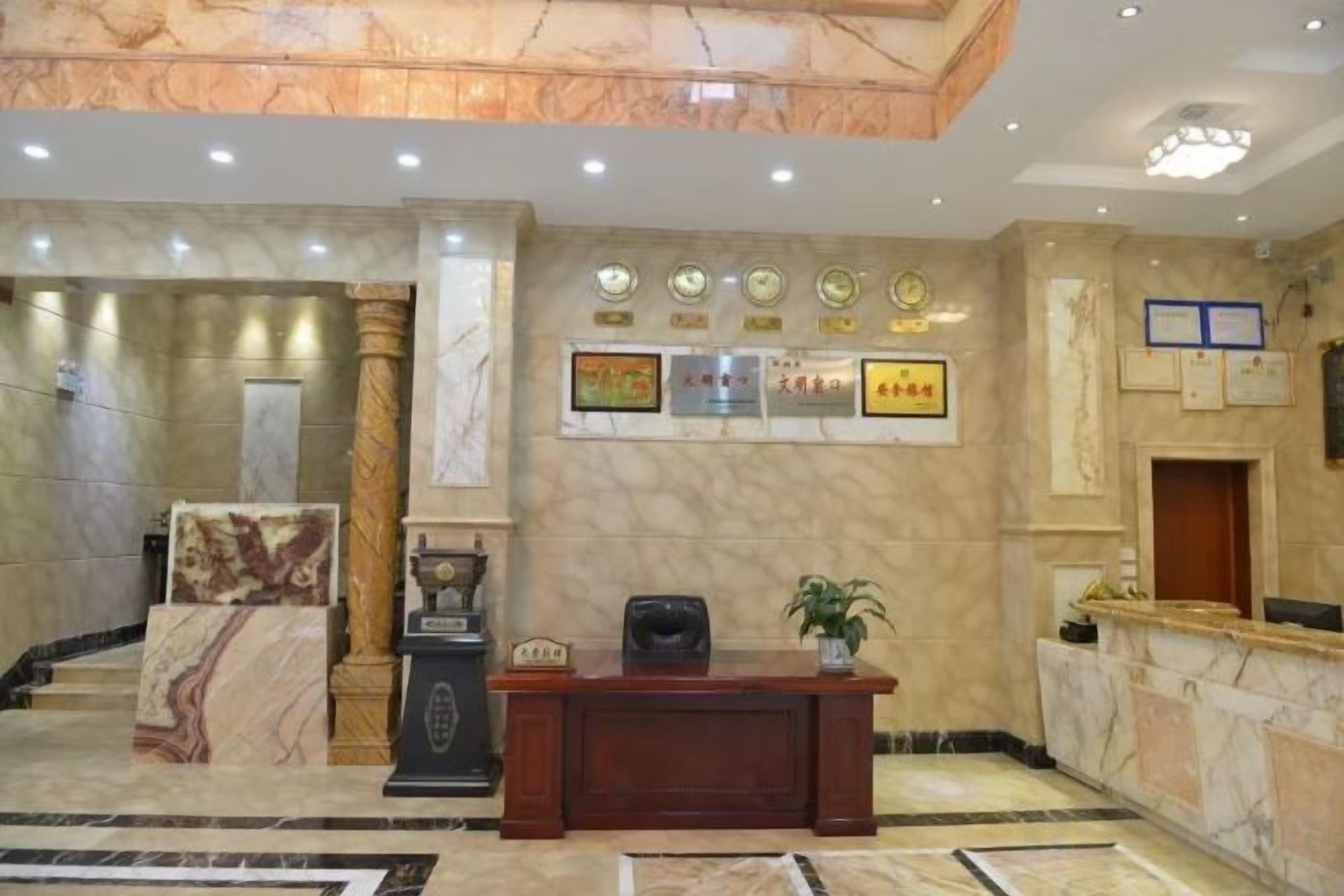 A reception area with a marble floor, a reception desk, a potted plant, and framed awards on the wall.