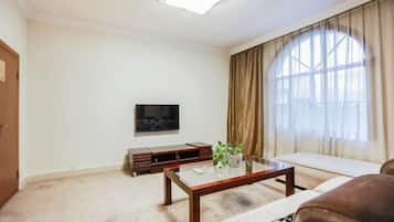 A living room with a sofa, a coffee table, a TV, and a large window with curtains.