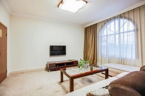 Una sala de estar con un sofá, una mesa de centro, un televisor y un ventanal con cortinas.