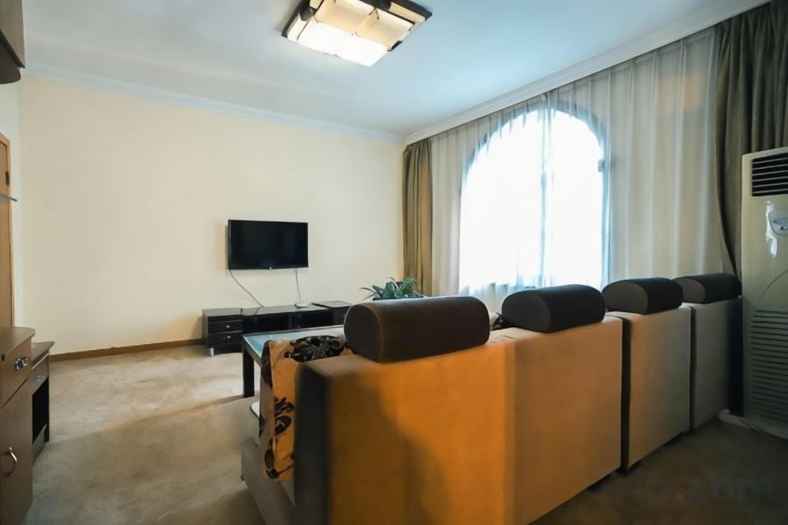 Una sala de estar con sofá, televisor de pantalla plana y un amplio ventanal con cortinas.