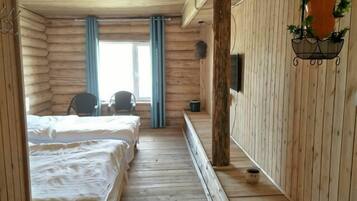 A log cabin room with two beds, a chair, a TV, and a window with curtains.