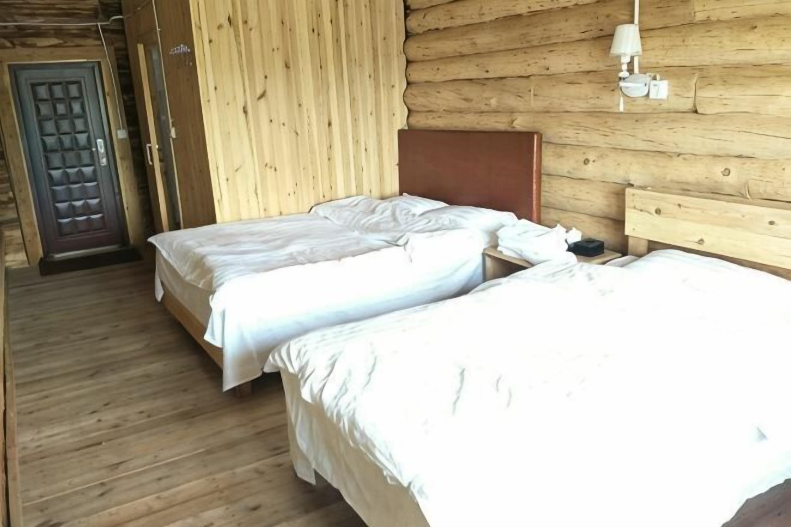 En træhytte med to senge, en dør og en vægmonteret lampe.