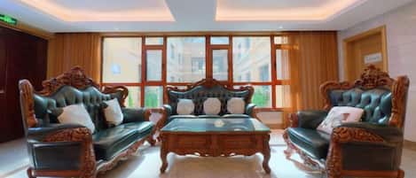 A lobby with two ornate sofas and a coffee table, large windows, and a tiled floor.