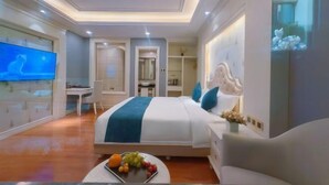 A modern hotel room with a large bed, a television, a desk, and a dining area with fruit. - Mintai Hot Spring Holiday Hotel (Zibo)
