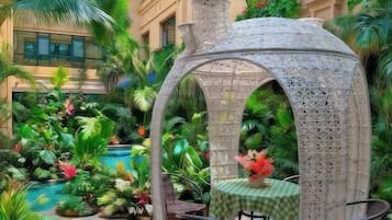 Ein Pavillon mit aufwendigen Gitterstrukturen, umgeben von üppiger tropischer Vegetation und einem kleinen Pool.