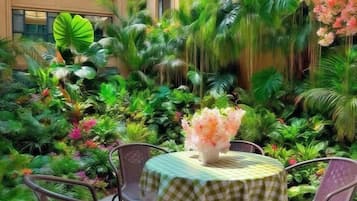 Ein runder Tisch mit kariertem Tuch und Stühlen, umgeben von üppigen tropischen Pflanzen und Blumen.