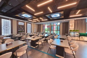 Un salón de conferencias con varias mesas y sillas, una larga mesa con un proyector y un ventanal con vistas.