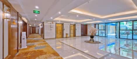 Un pasillo de hotel con piso pulido, una recepción y un ventanal grande a la derecha.
