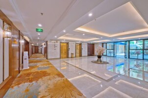 Un pasillo de hotel con piso pulido, una recepción y un ventanal grande a la derecha.