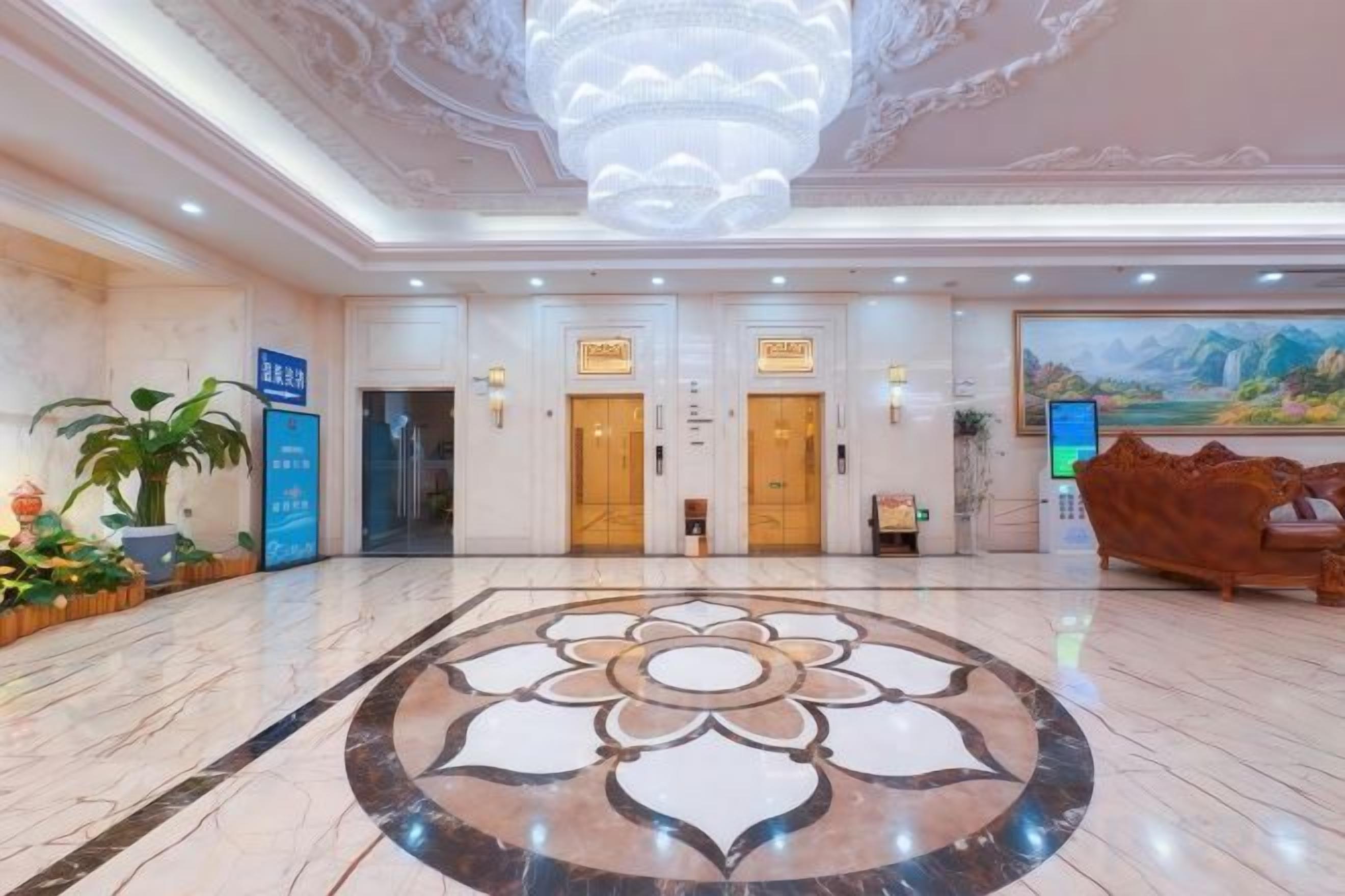 Vestíbulo de hotel con piso de mármol, un candelabro, mostradores de recepción y un cuadro grande en la pared.