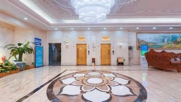 Vestíbulo de hotel con piso de mármol, un candelabro, mostradores de recepción y un cuadro grande en la pared.