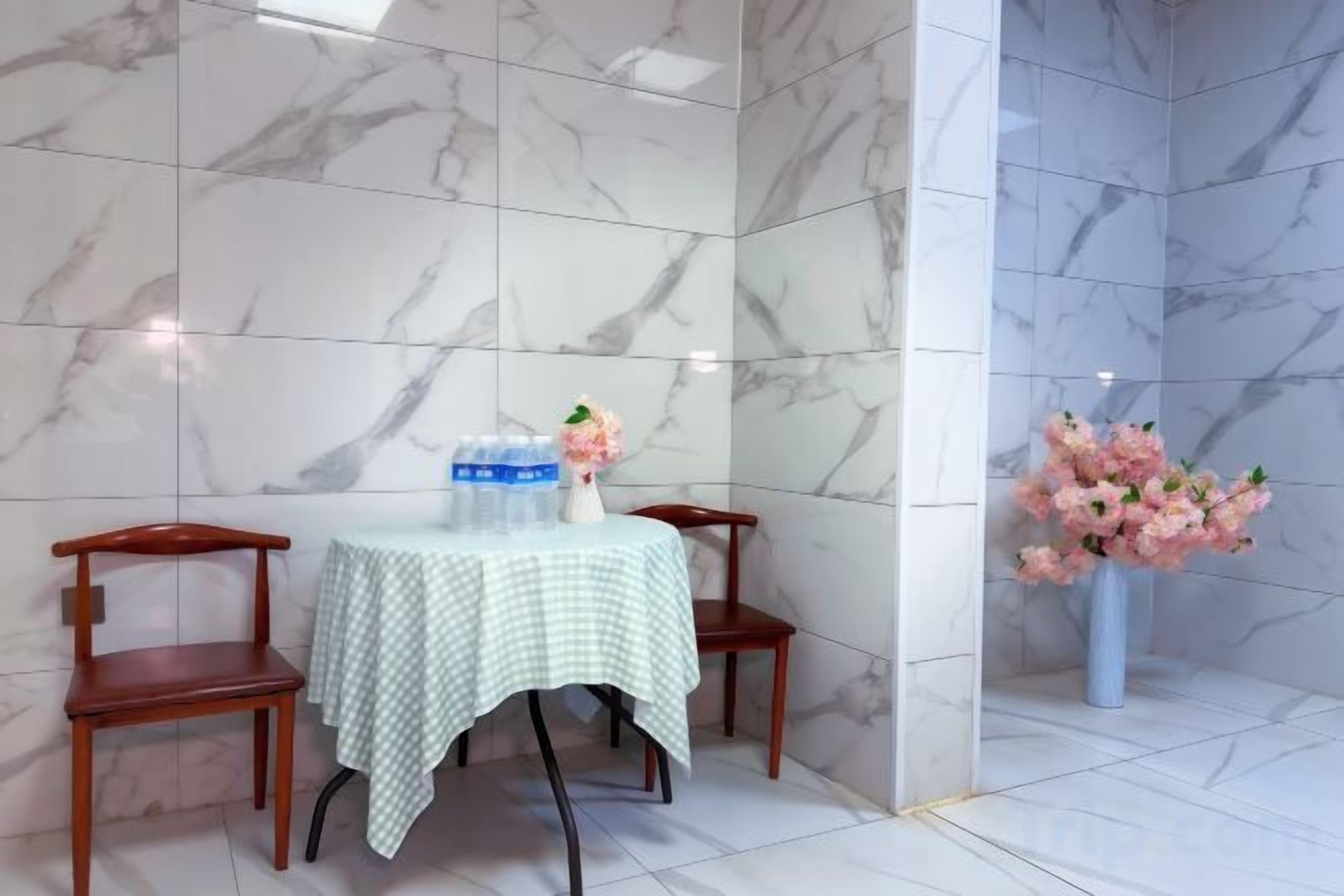 Ett rum med en vägg av marmor, ett bord med ett rutigt bordsduksöverdrag, två stolar, en vas med blommor och en vattenautomat.