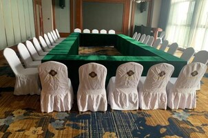 Un salón de conferencias con una mesa larga, sillas blancas y un mantel verde.