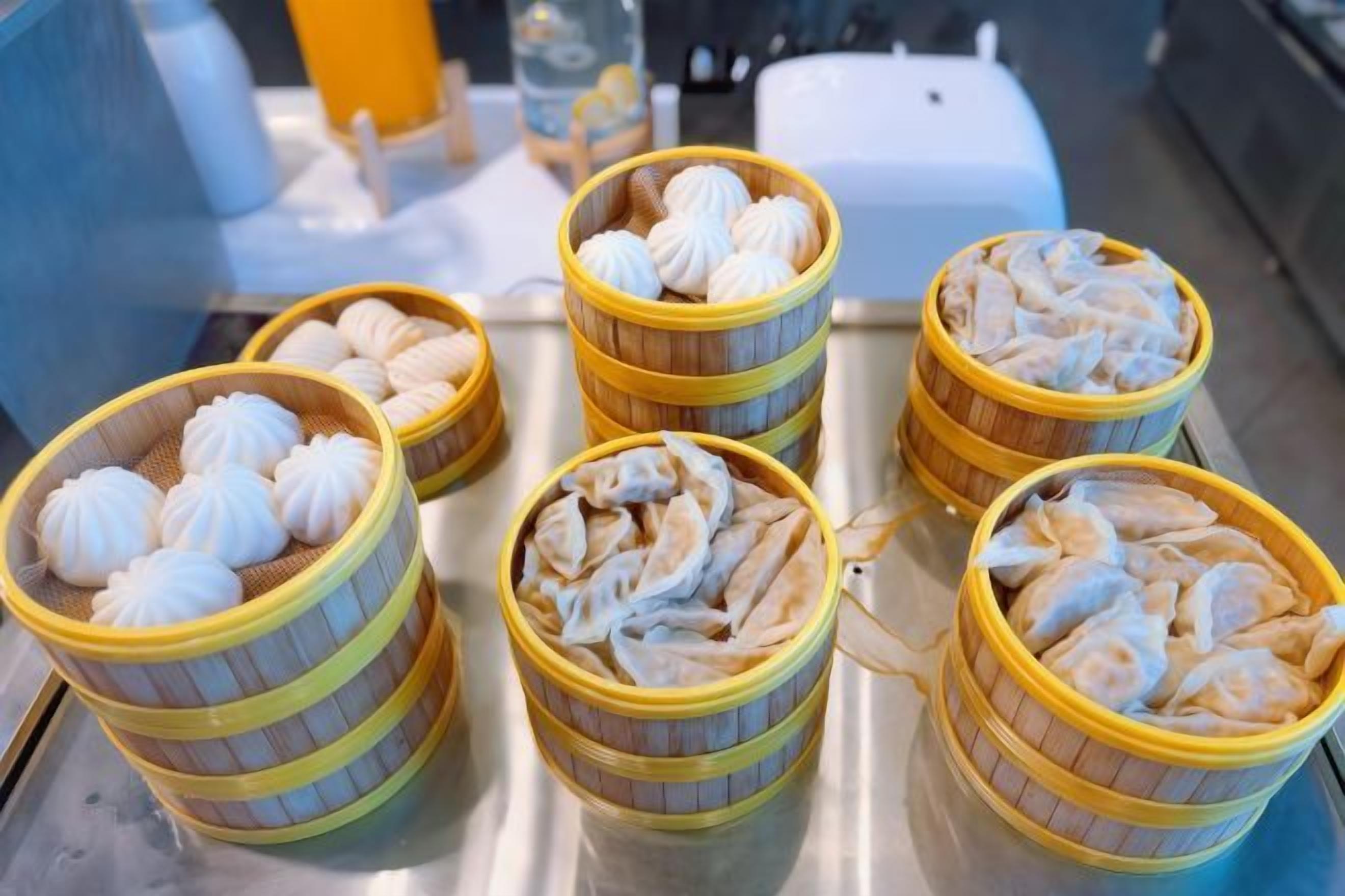 Four bamboo steamers with dumplings on a stainless steel surface.