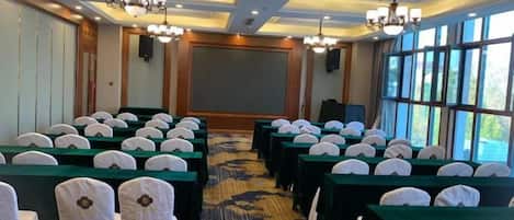 Un salón de conferencias con filas de mesas y sillas, una pantalla grande y un candelabro.