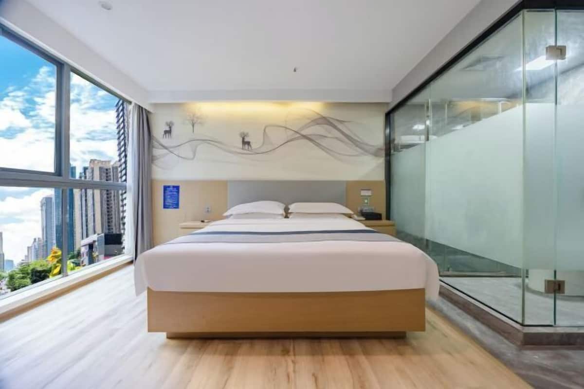 A modern bedroom with a large bed, a city view, and a glass partition wall.
