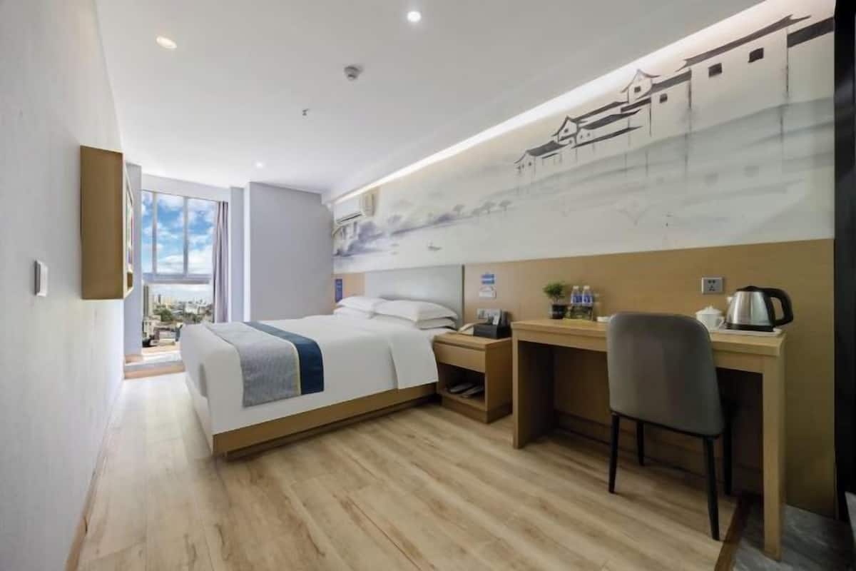 A hotel room with a bed, desk, chair, and a mural on the wall.