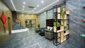 Un hall d’entrée moderne avec un sol en marbre, un escalier, un espace détente avec des canapés et une étagère en bois agrémentée de plantes.