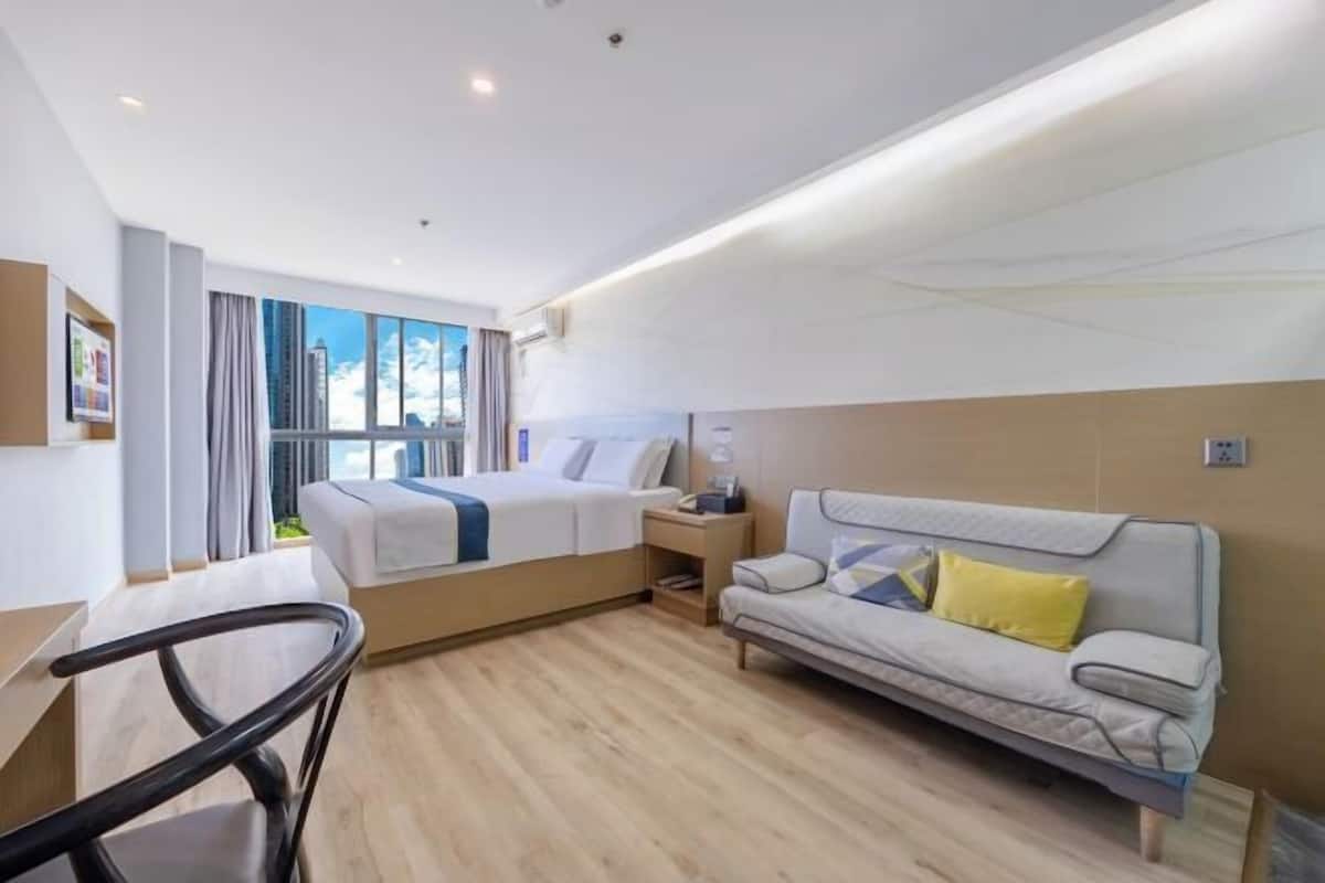 A modern hotel room with a bed, a sofa, a desk, and a chair.