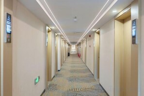 A hotel corridor with doors on both sides, a patterned carpet, and a ceiling light fixture.