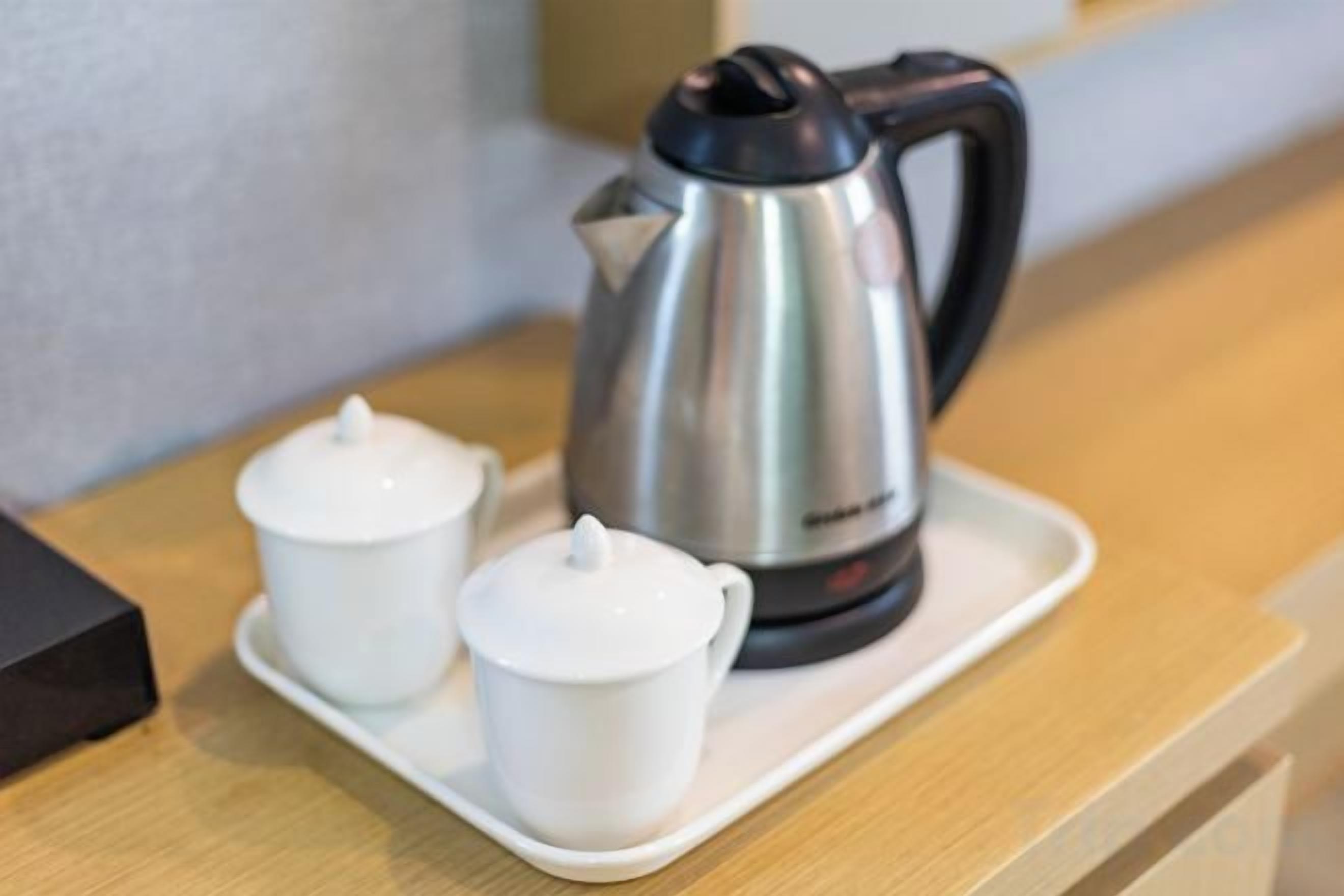 Una tetera de acero inoxidable y dos tazas de té blancas sobre una bandeja.