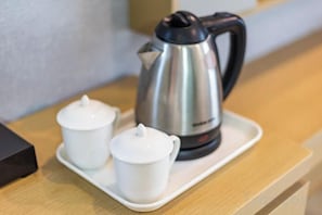 A stainless steel kettle and two white teacups on a tray.