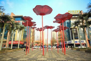 A plaza with red umbrella-like structures, palm trees, and modern buildings in the background.
