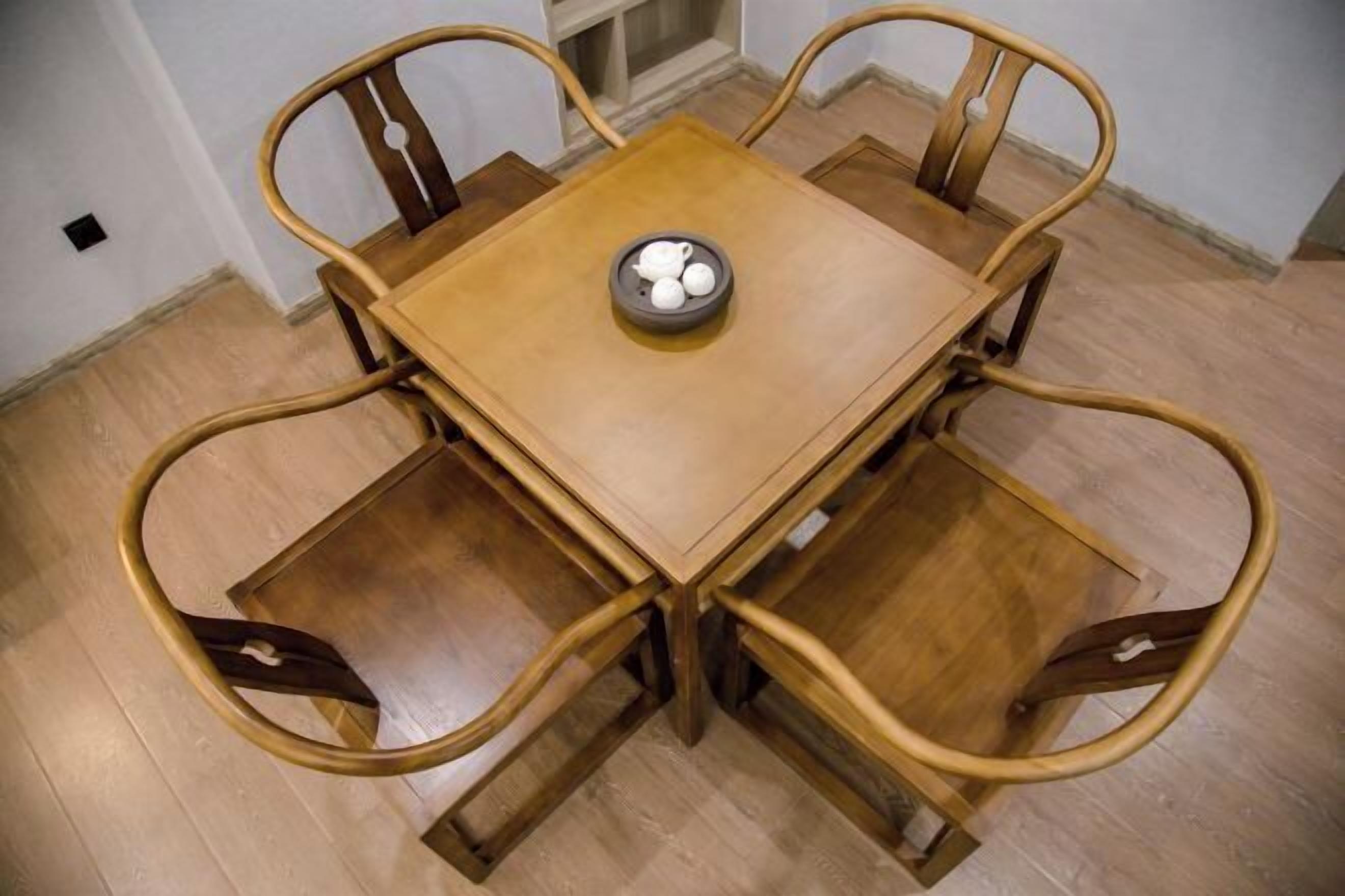 A square wooden table with four chairs, each with a curved backrest. A small bowl with a lid is placed on the table.