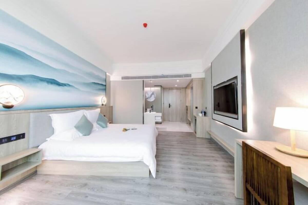 A modern hotel room with a bed, a TV, a desk, and a bathroom visible through an open door.