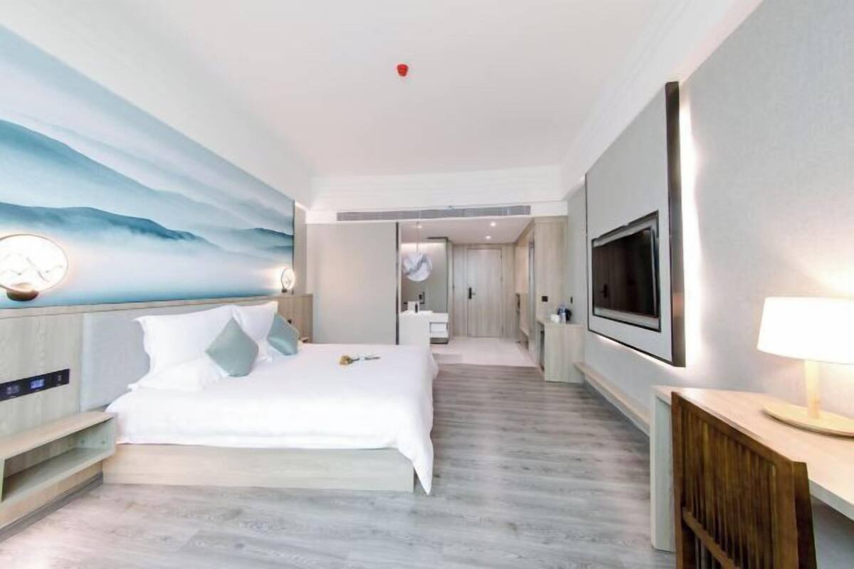 A modern hotel room with a bed, a TV, a desk, and a bathroom visible through an open door.