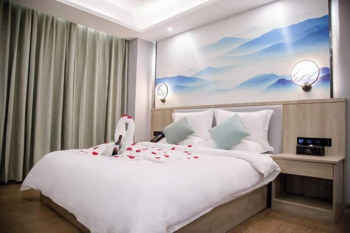 A hotel room with a bed, a nightstand, a wall clock, and a painting.