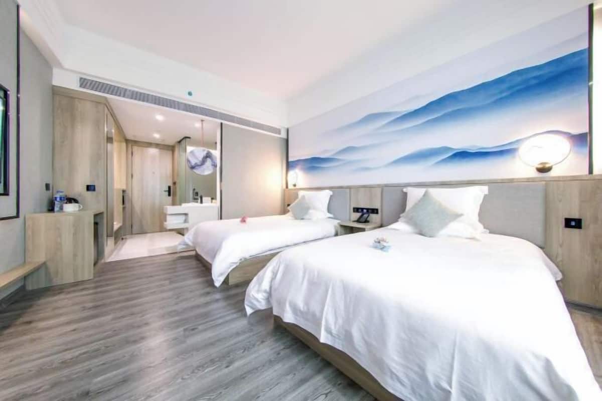 A hotel room with two beds, a wooden floor, a large wall mural, and a bathroom visible through an open door.