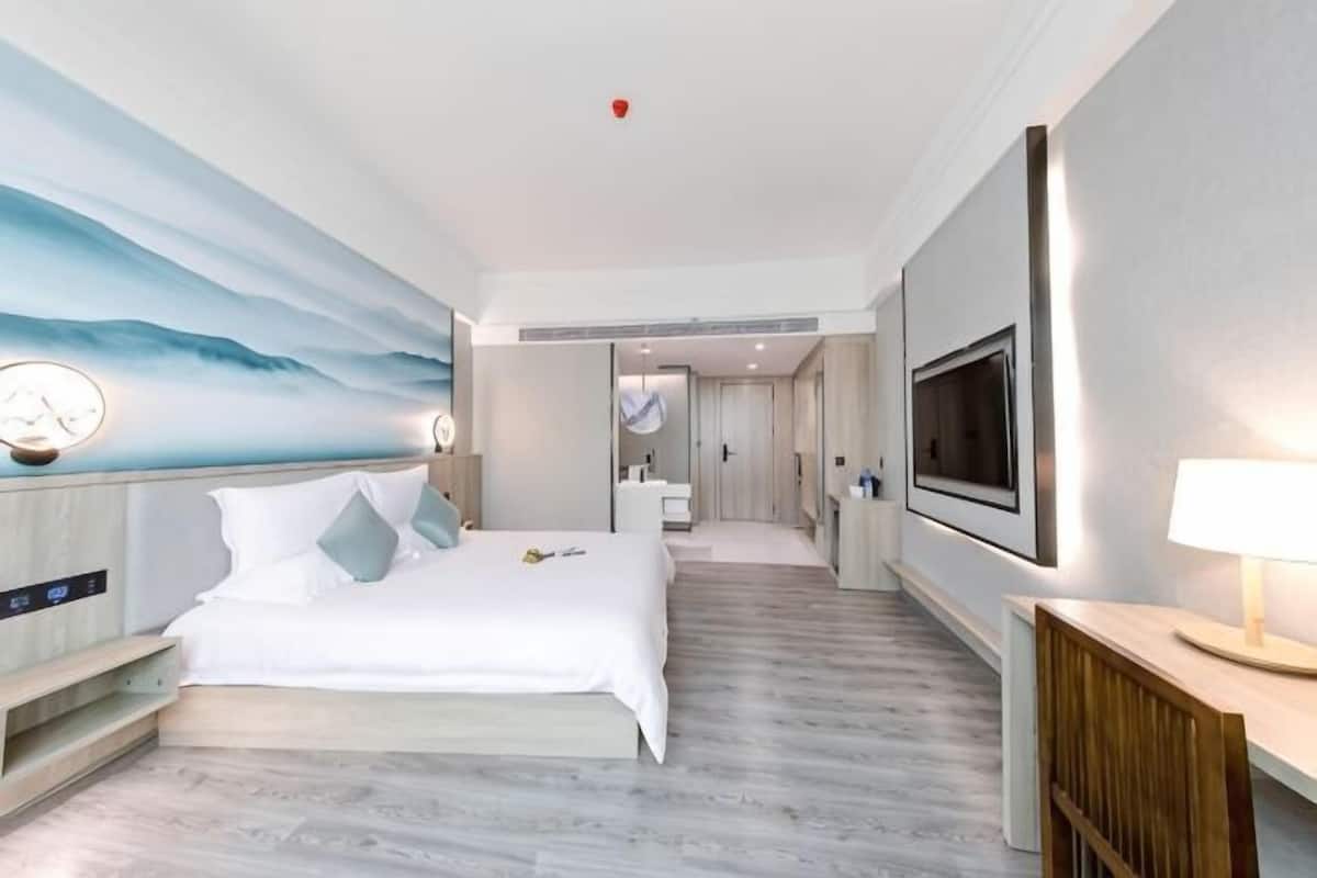 A hotel room with a bed, a TV, a desk, a lamp, a painting, and a bathroom.