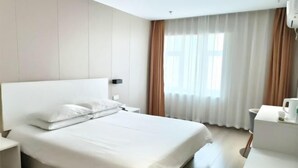 A hotel room with a large bed, a bedside table, a nightstand, a window with curtains, and a wall-mounted air conditioning unit. - Homeinn Pebble Hotel (Hami Railway Station Bayi North Road) (Hami)