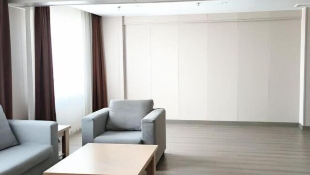 A modern hotel room with a grey sofa, a wooden coffee table, and a large window with curtains. - Homeinn Pebble Hotel (Hami Railway Station Bayi North Road) (Hami)