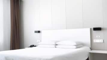 A modern hotel room with a large bed, white linens, and a headboard with a flat panel design.