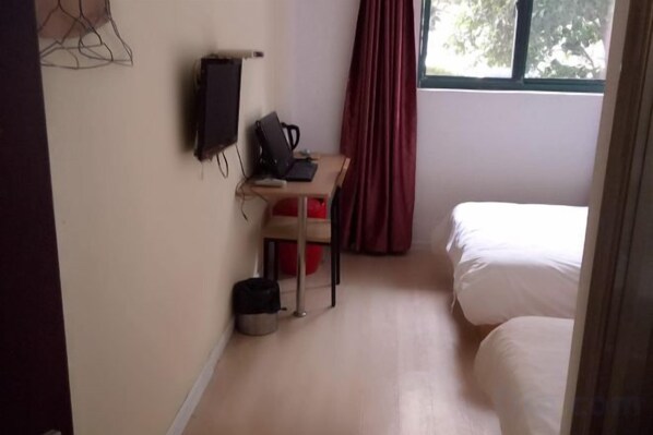 Une chambre à coucher avec un lit, un bureau et une chaise, une télévision et une fenêtre avec des rideaux.