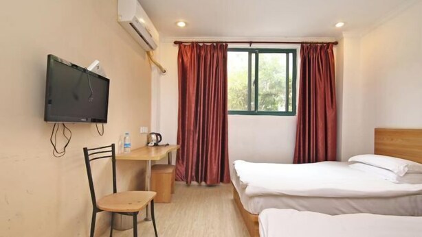Une chambre d’hôtel comprenant un lit, un bureau avec une chaise, une télévision et une fenêtre avec des rideaux.