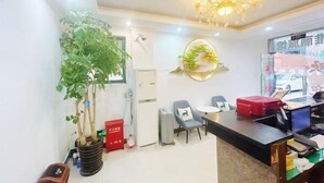 Un espace d’accueil d’hôtel comprenant un comptoir, des chaises, une plante en pot, un lustre et un élément décoratif mural.