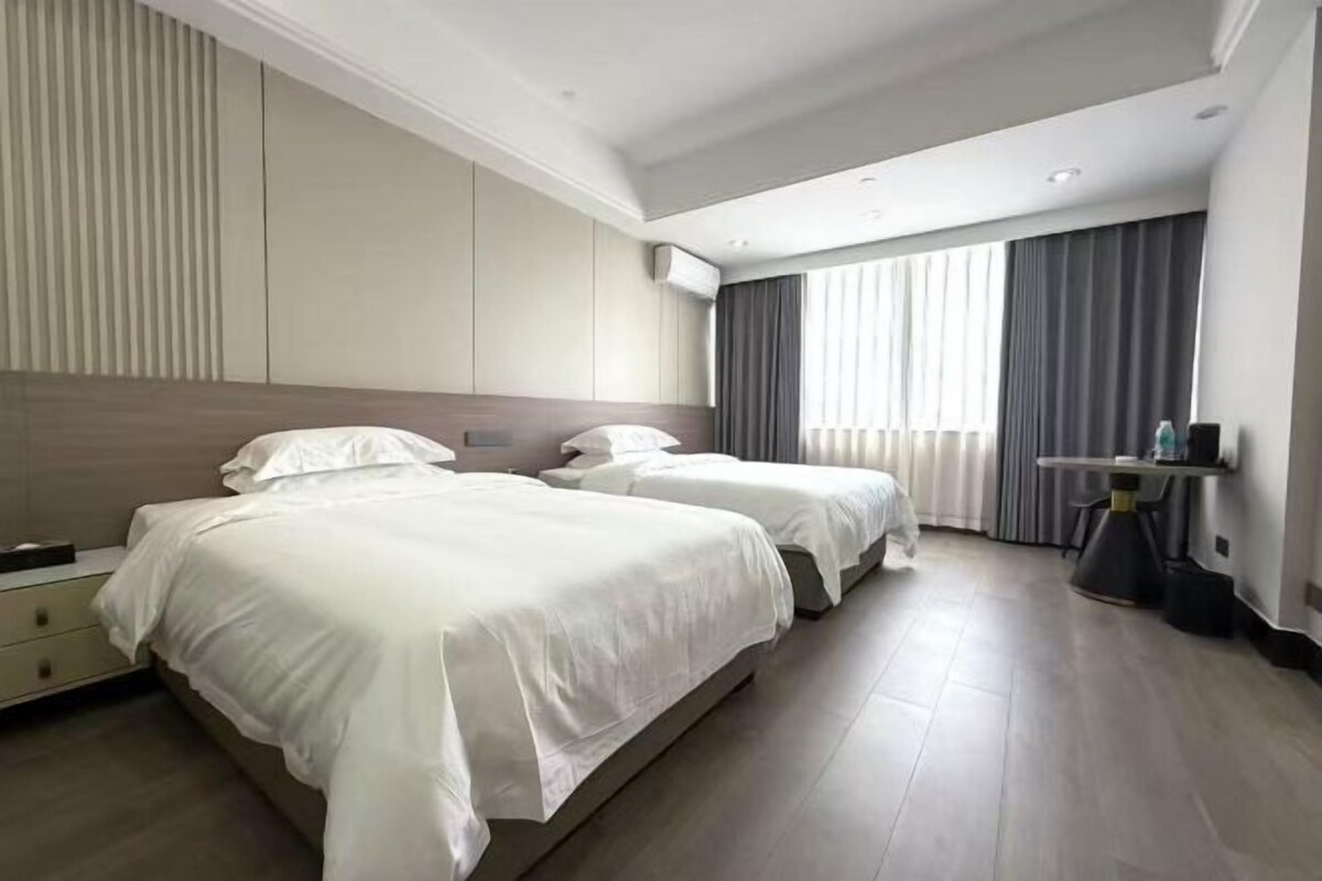 A hotel room with two beds, a bedside table, a desk, and a window with curtains.