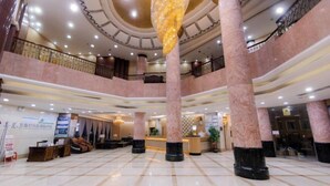 Un amplio vestíbulo con columnas de mármol, una recepción y un techo alto con iluminación empotrada.