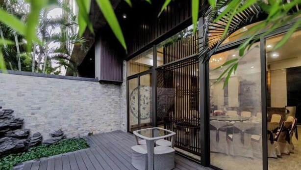 Un patio moderno al aire libre con un muro de piedra, una terraza de madera y una zona de estar con mesa y sillas.