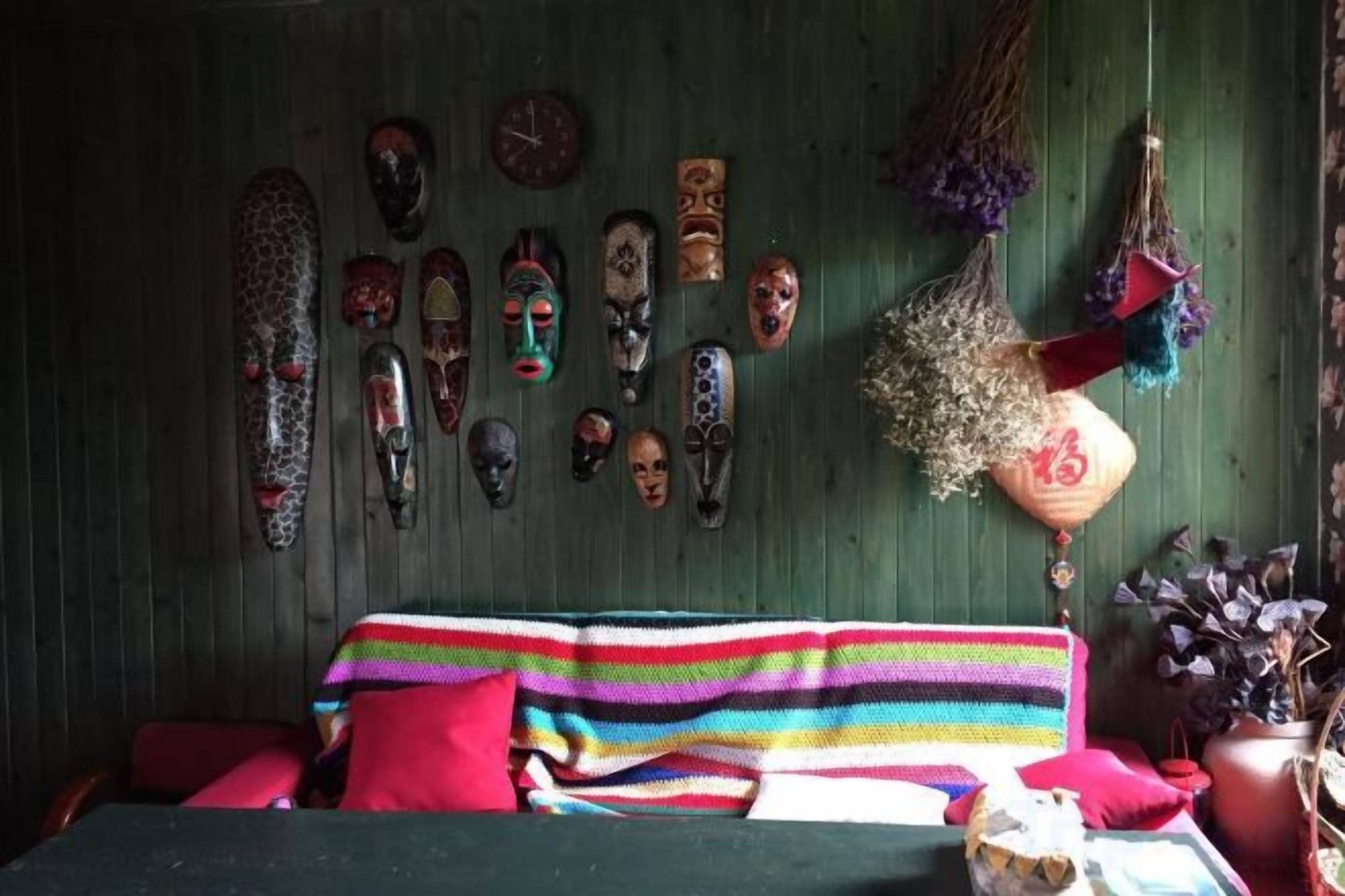 A room with a bed, a wall decorated with various masks, and a hanging plant.