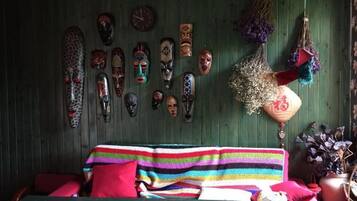 A room with a bed, a wall decorated with various masks, and a hanging plant.